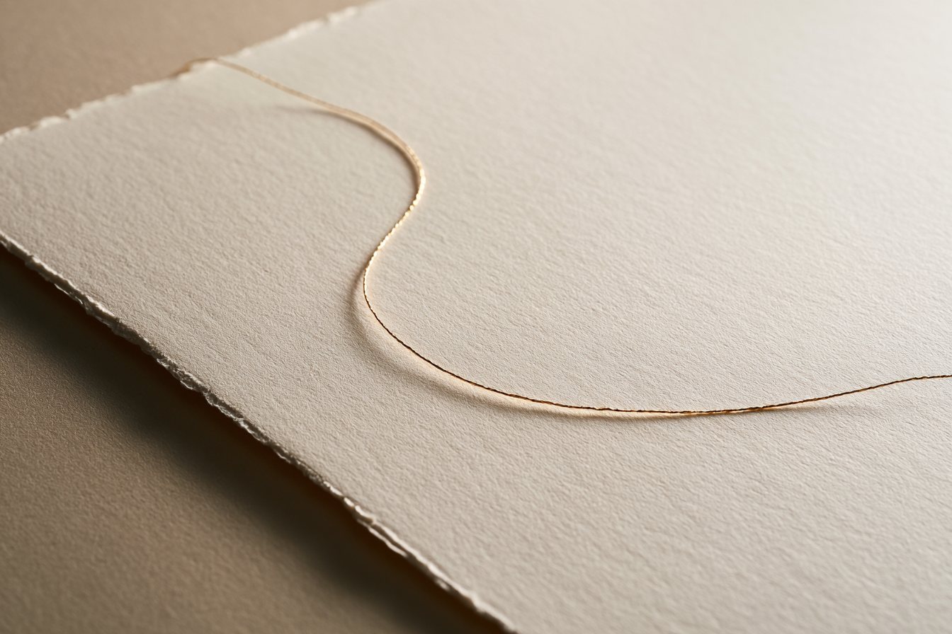 A single fine gold thread curving across heavy cream paper with a deckled edge